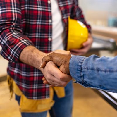 Roofing contractor shaking hands with customer while holding yellow hard hat