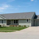 Long single story home with light siding and a dark shingle roof
