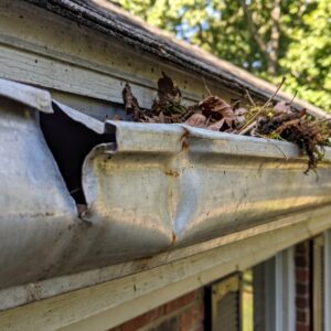 A dented gutter section clogged with leaves and debris