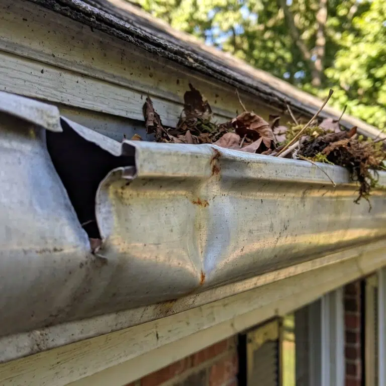 A dented gutter section clogged with leaves and debris